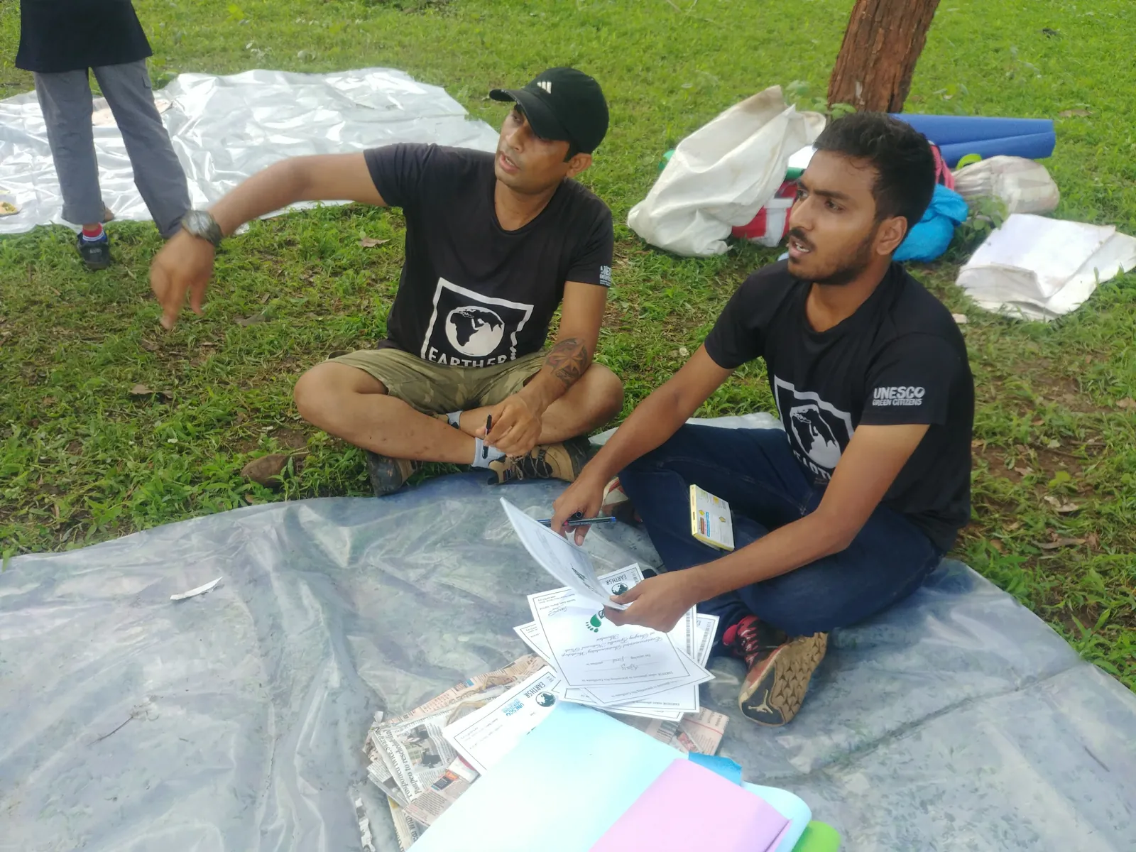 Two Earth5R volunteers recording waste audit data on a tarp with sorted waste