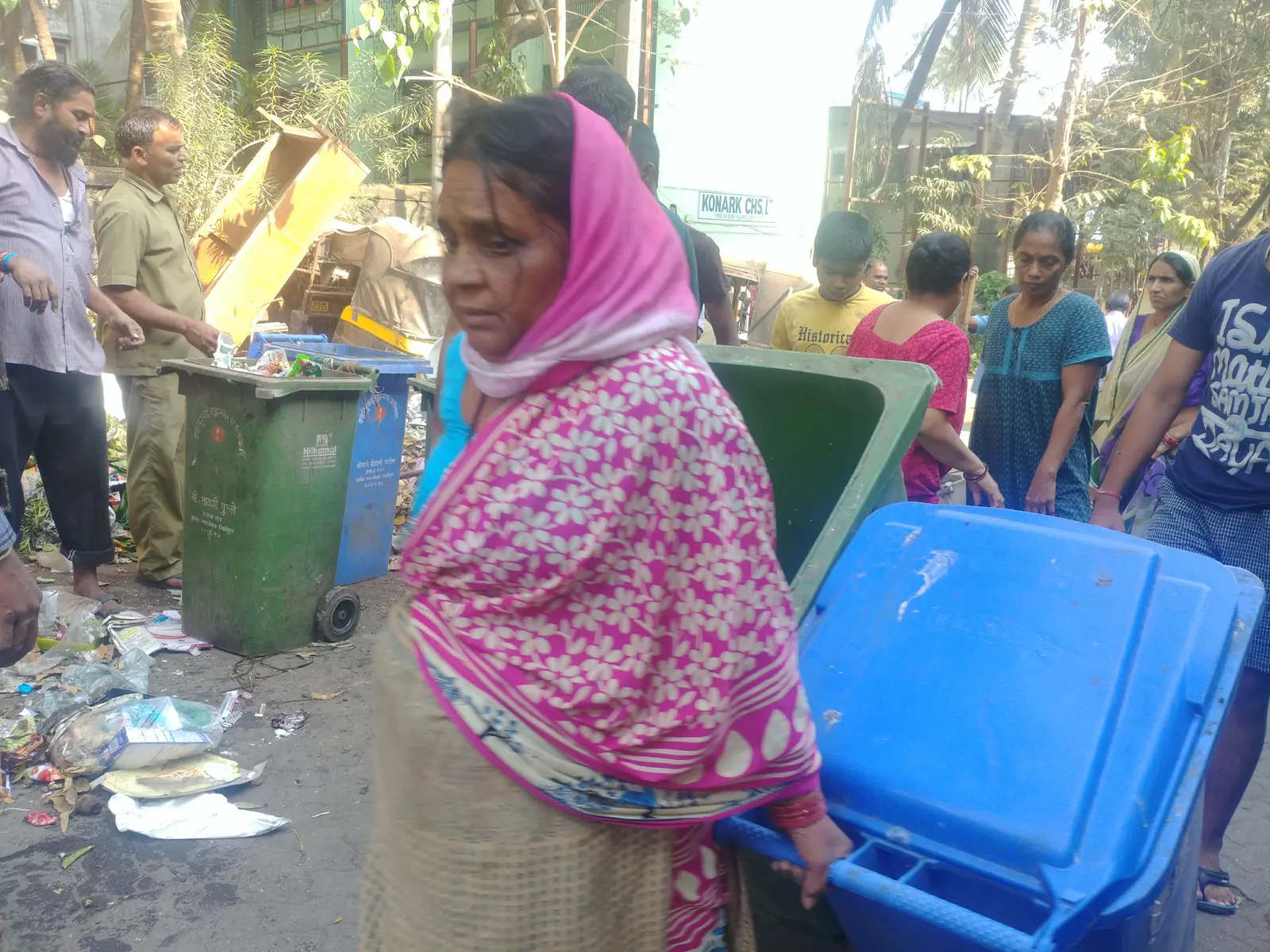 Environmental law internship field work. Woman in a pink headscarf beside new green and blue bins for segregated waste