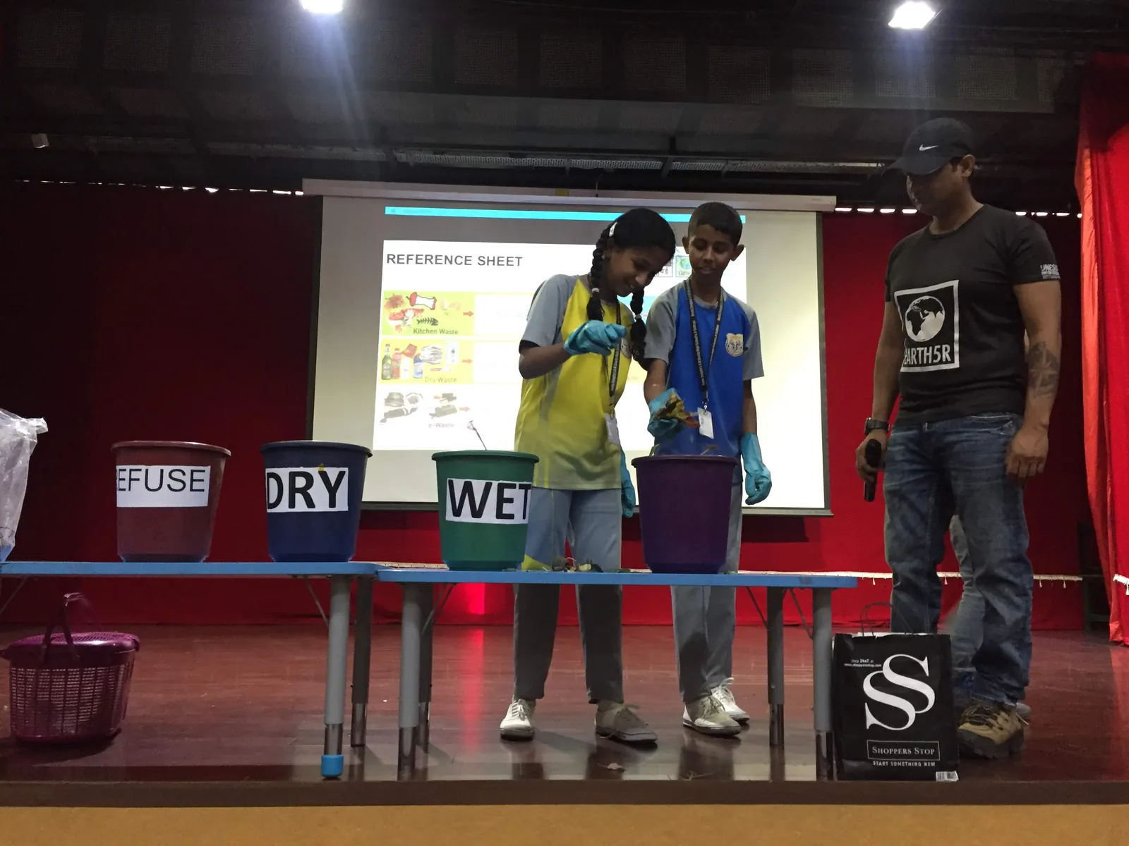 High school public policy internship field work. Students on stage taking part in a waste segregation demonstration with colour-coded bins