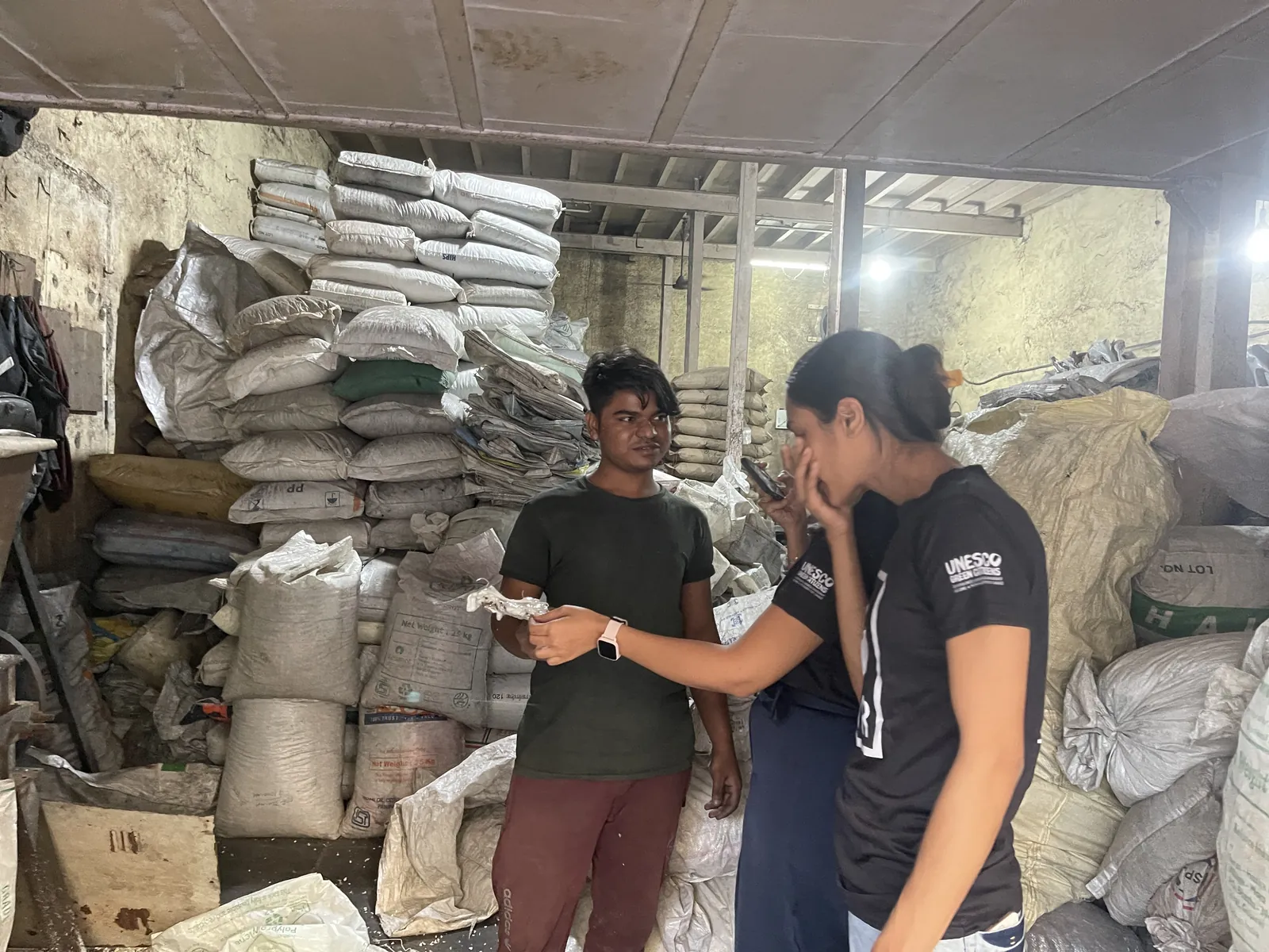 Earth5R volunteers talking with a worker in a scrap godown stacked with sacks
