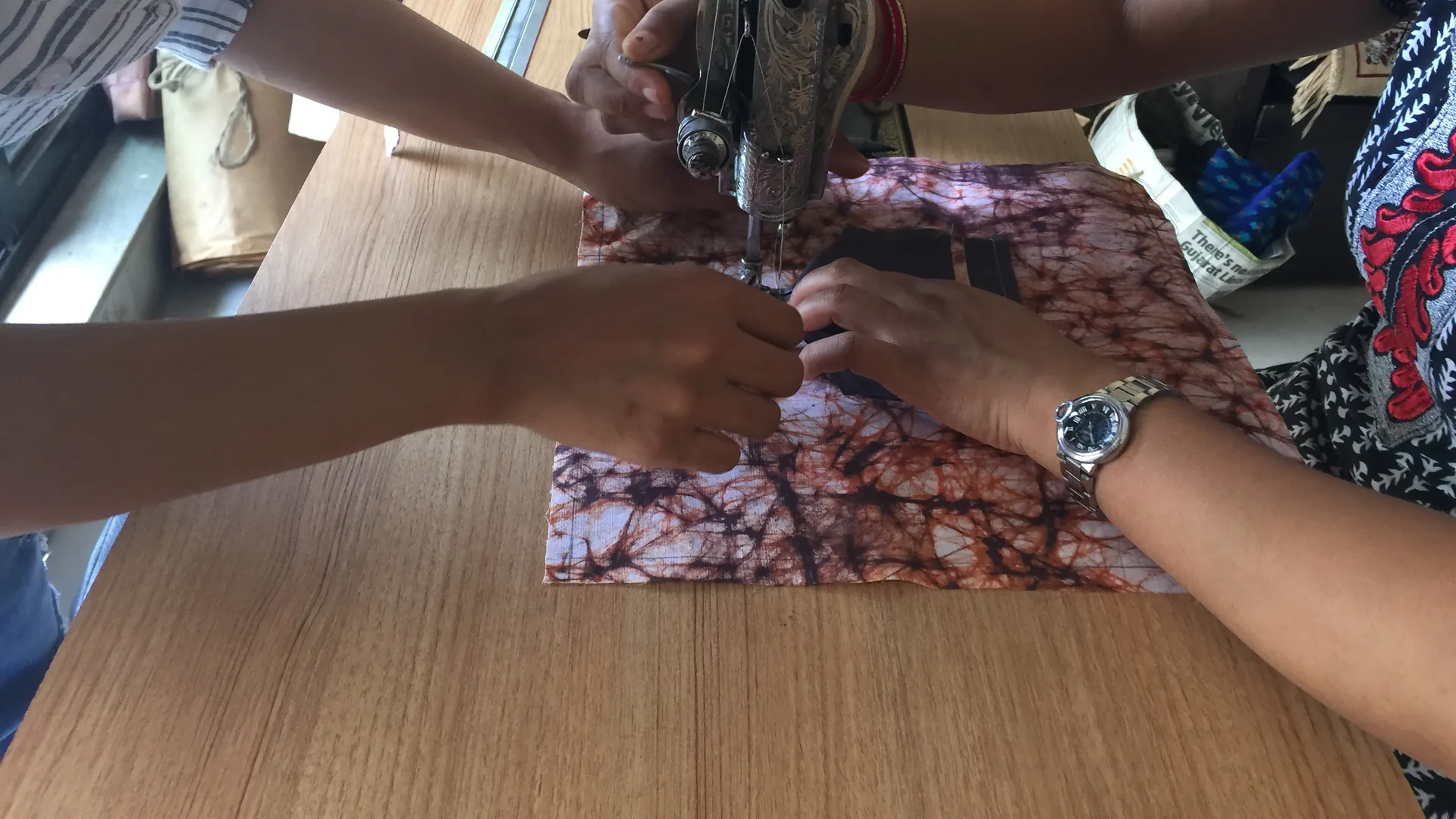 Two pairs of hands guiding a piece of printed cotton fabric through a sewing machine during an Earth5R upcycling session