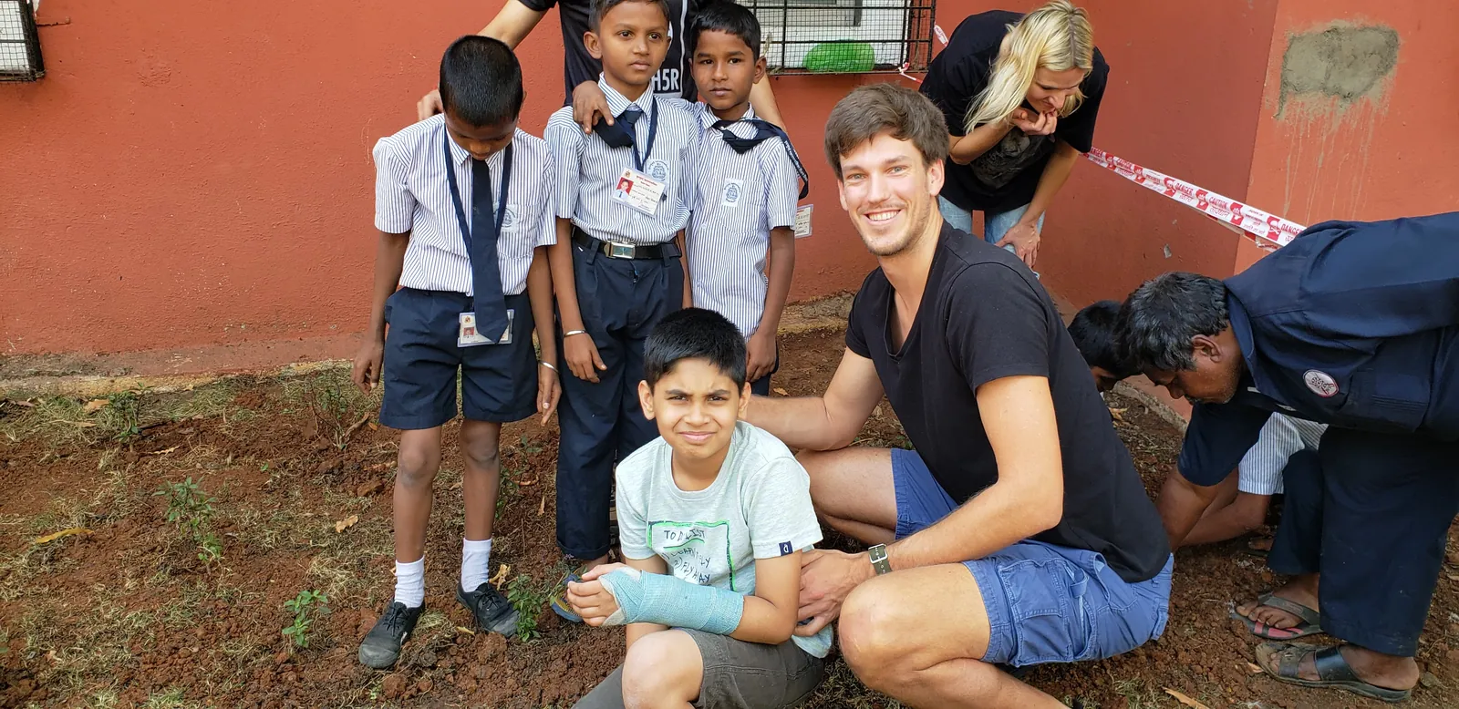 High school agriculture internship field work. Earth5R volunteer kneeling with schoolboys in the school garden during a planting session