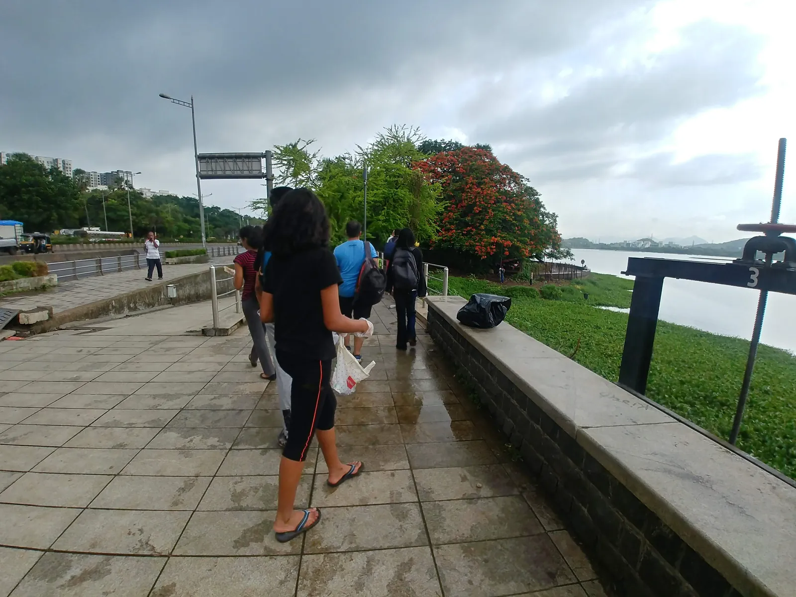 High school water resources internship field work. Volunteers walking along a lakeside promenade on a cloudy monsoon day