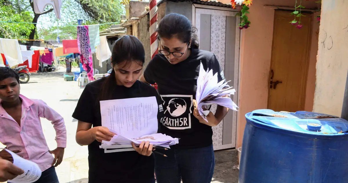 Two young Earth5R volunteers reviewing community survey forms together in a residential lane